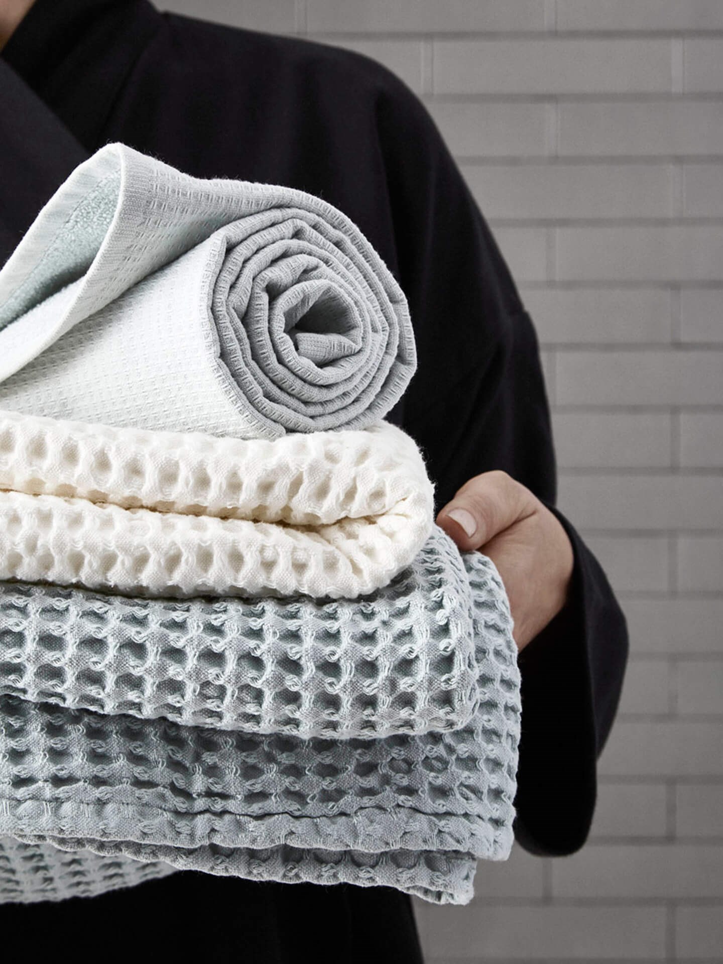 Miljøbilde badehåndklær bomull. Big waffle towel and blanket i hvit fra The Organic Company. Holdes av dame i morgenkåpe.